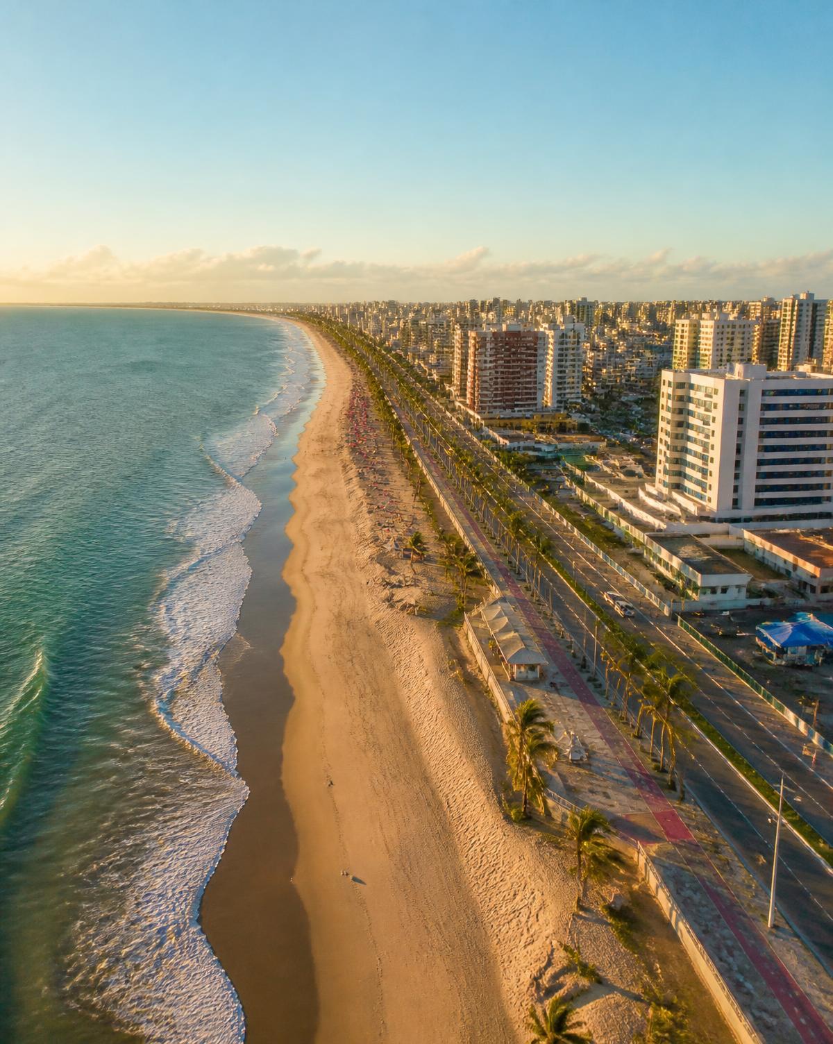 Vista aérea da orla de Aracaju, em Sergipe, com praia, mar azul e coqueiros ao pôr do sol